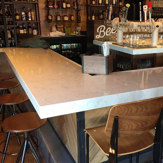 A bar with a white stone countertop and wooden stools.