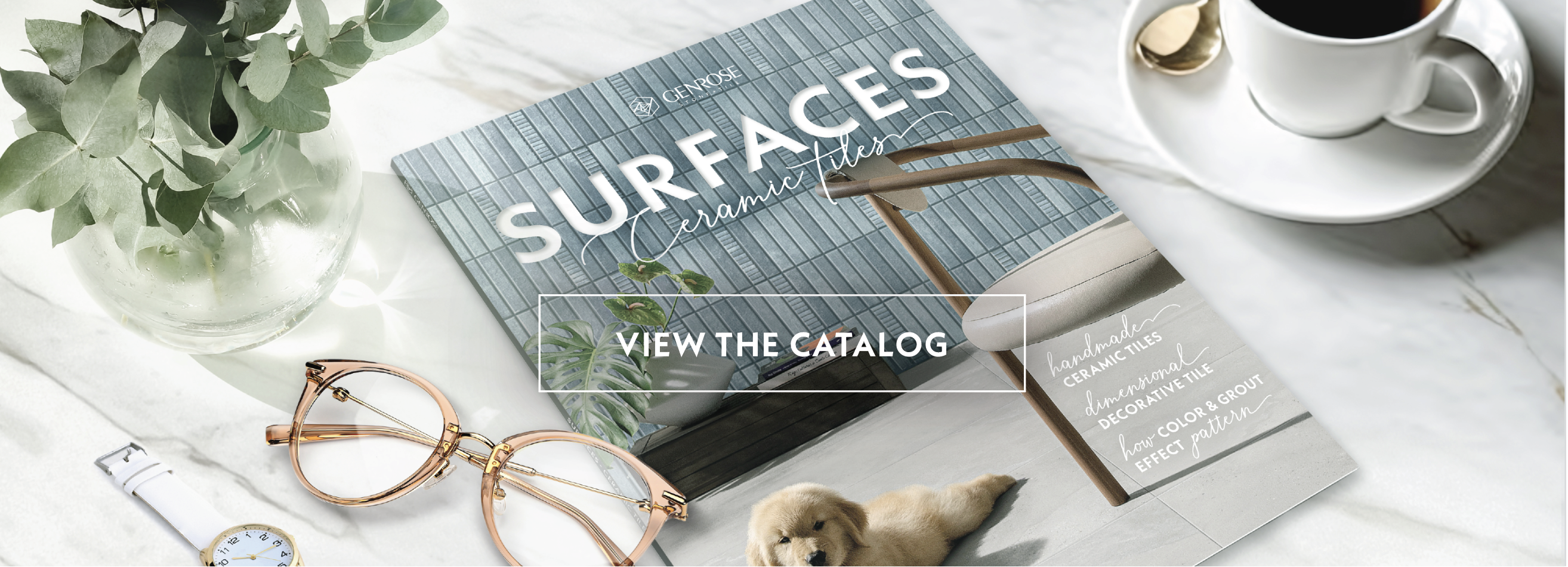Catalog with blue and gray tiles, glasses, plant, coffee, and a puppy. Text: "SURFACES ceramic tile" and "VIEW THE CATALOG."