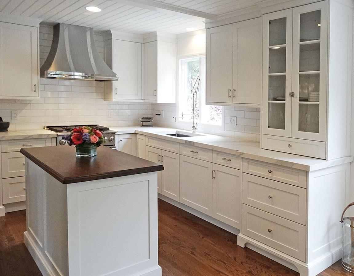 Modern kitchen with white cabinets, white countertops, and a dark wood island top.