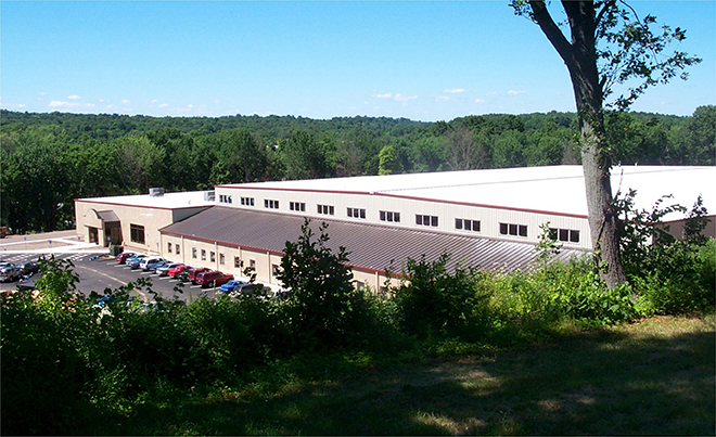 Large beige and red building with a parking lot, surrounded by greenery.