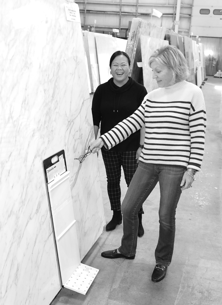 Two women examining a large white marble slab with gray veining.