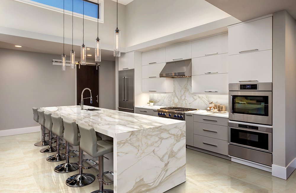 Modern kitchen with white and gold marble countertops and backsplash, light beige floor tiles, and stainless steel appliances.