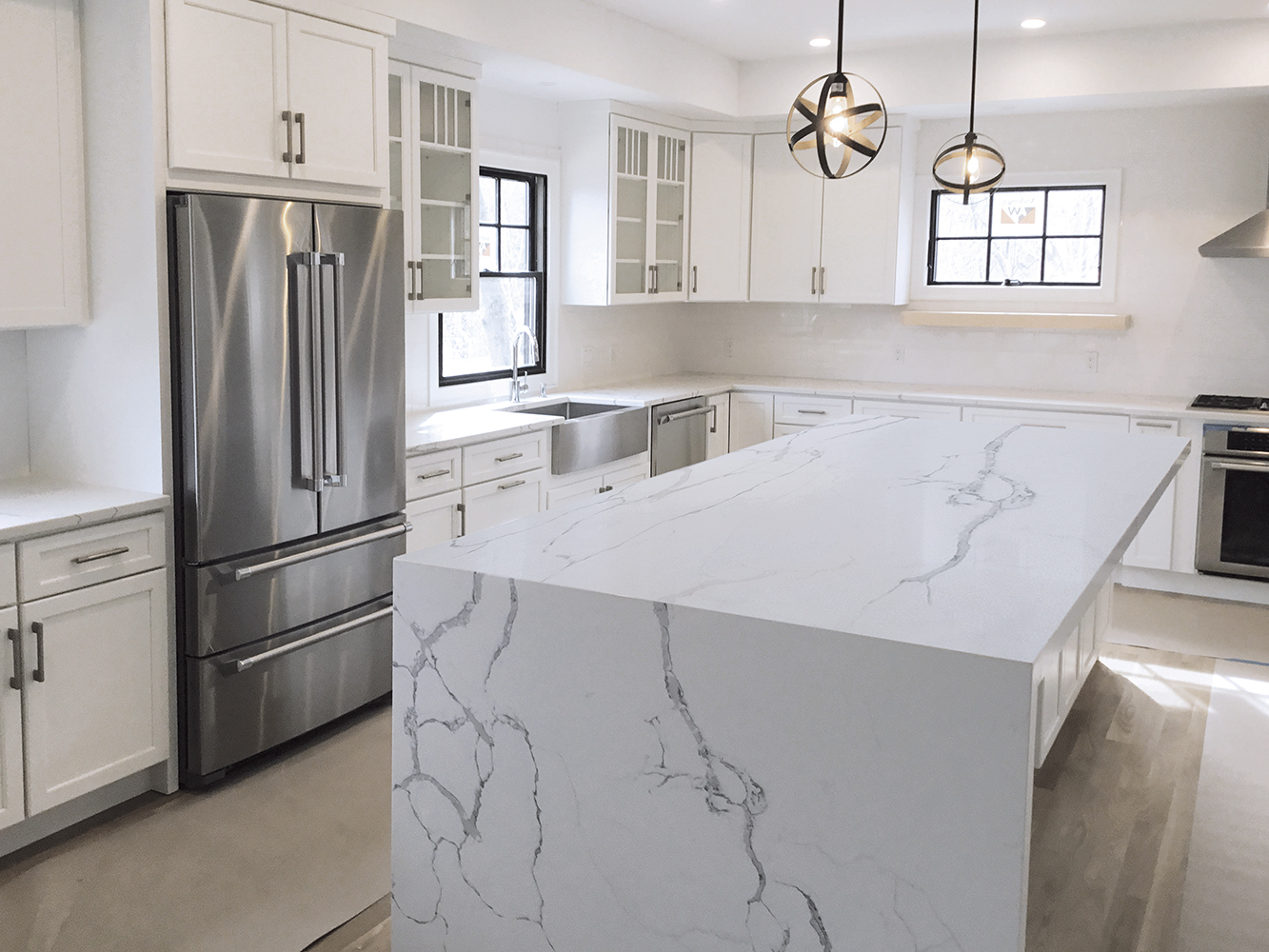 Modern kitchen with white marble-patterned porcelain waterfall countertop and stainless steel appliances.