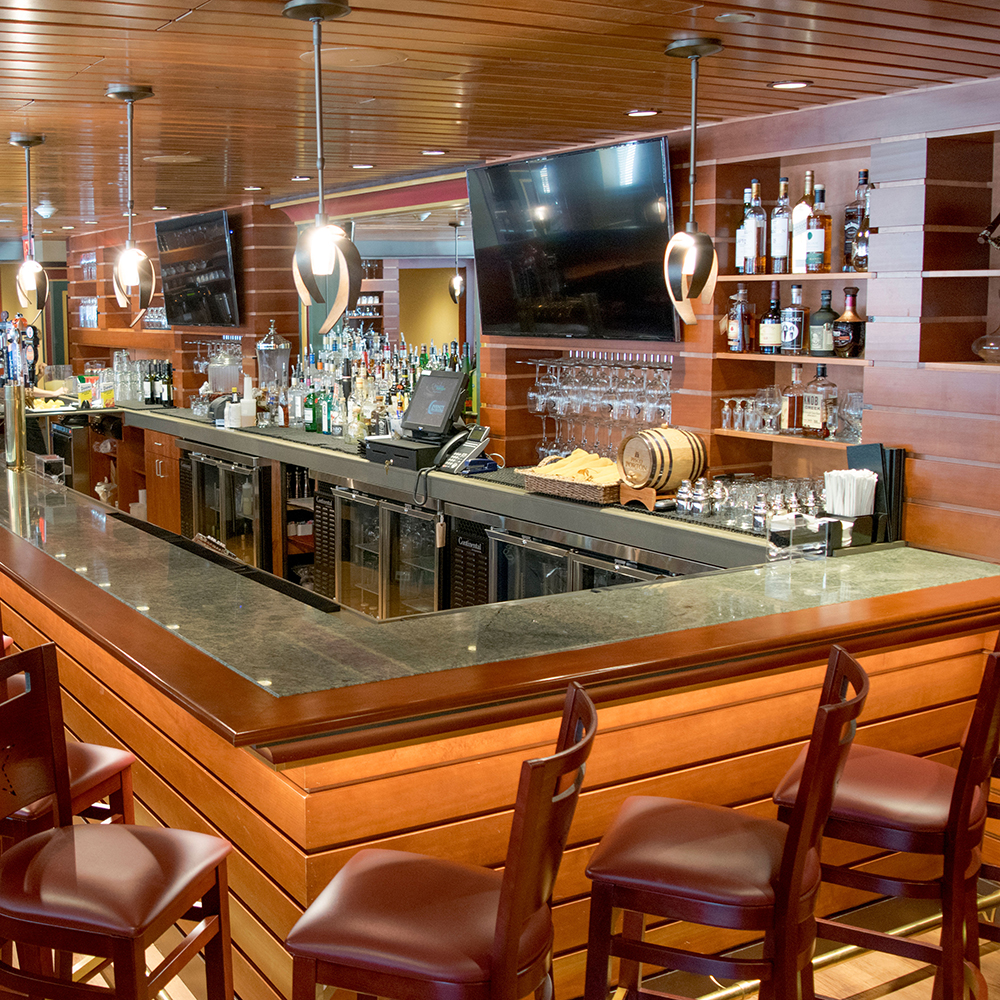 A bar with a polished stone countertop and wooden paneling, featuring bar stools and shelves with bottles.