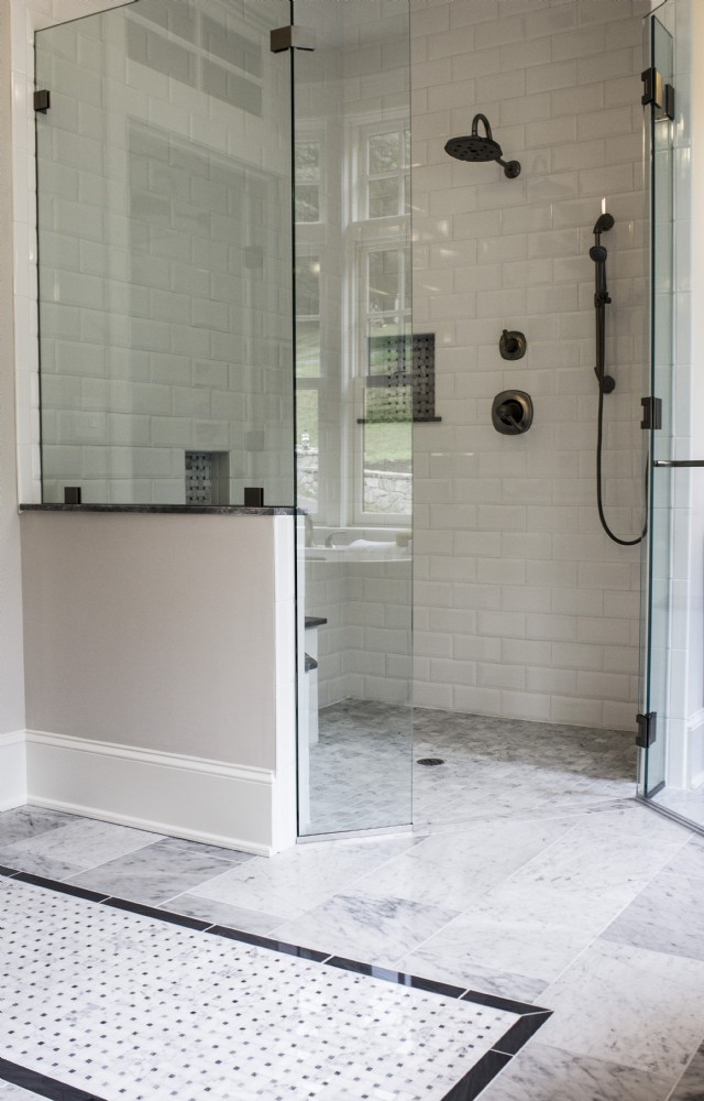 Glass shower with white subway tiles, black fixtures, and marble floor tiles.