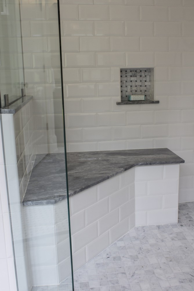 White tiled shower with a gray stone bench and niche.